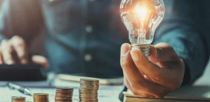 Hero image of a powered-on lightbulb next to several stacks of coins