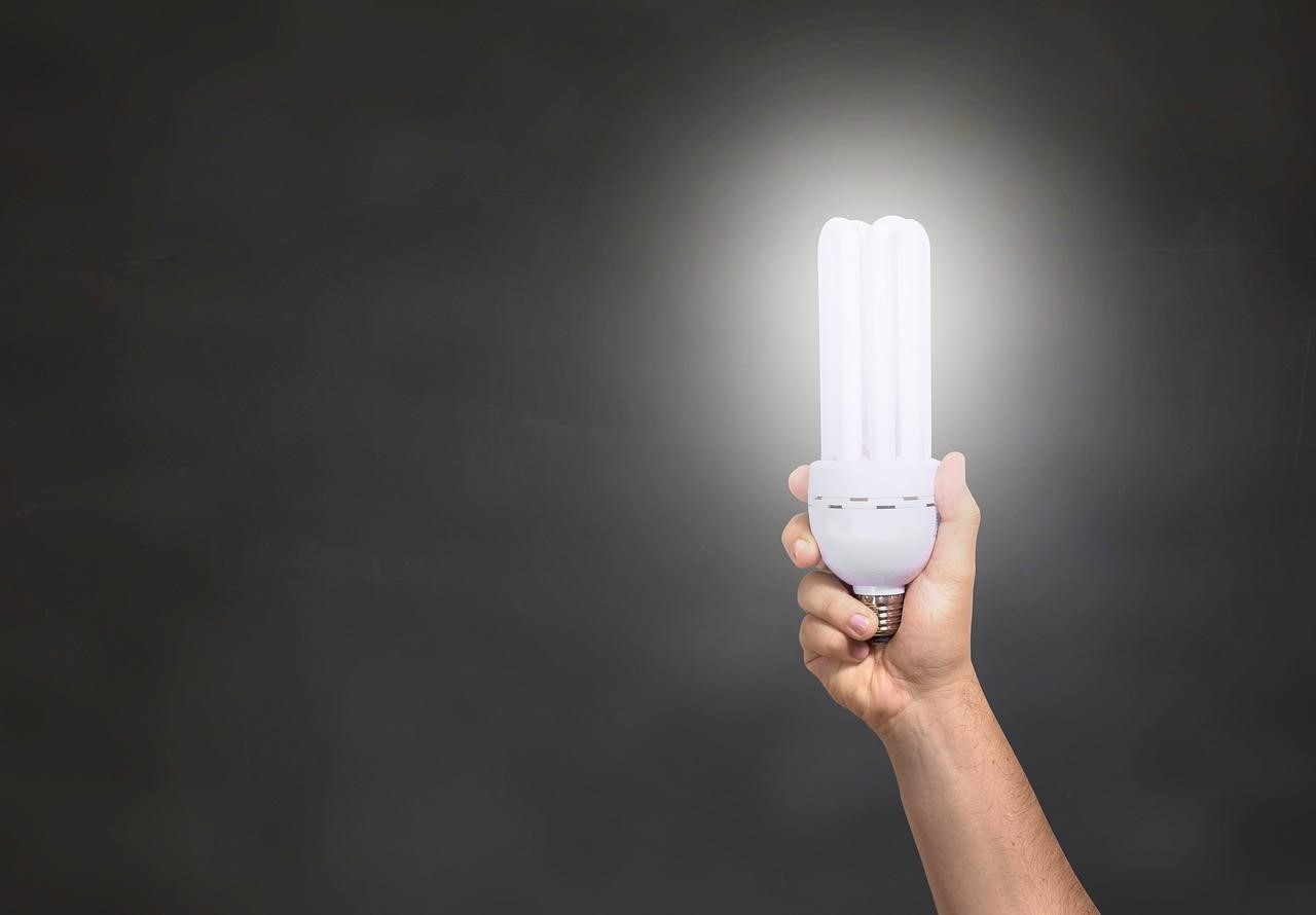 A hand holding an illuminated CFL light bulb