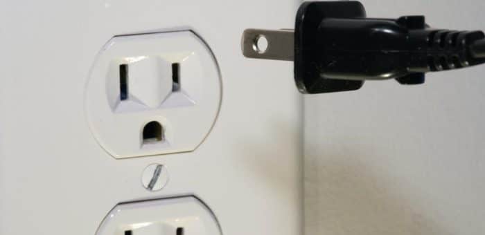 a white outlet with a black electrical cord about to be plugged in