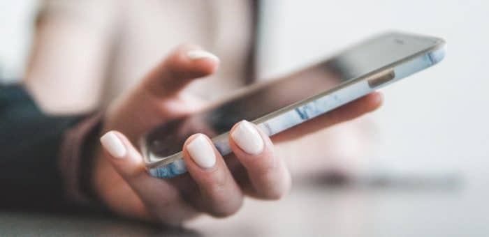 person's hand with pink nail polish holding an iphone