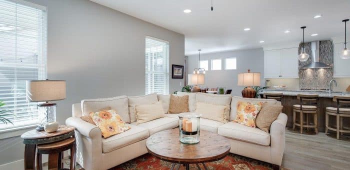 A living room with a big L shaped white couch and a kitchen in the background.