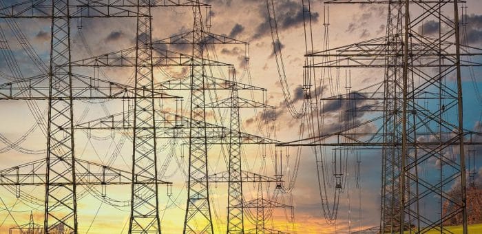 Towers with electricity lines with green grass on the ground and a yellow pink and blue sunset with gray clouds