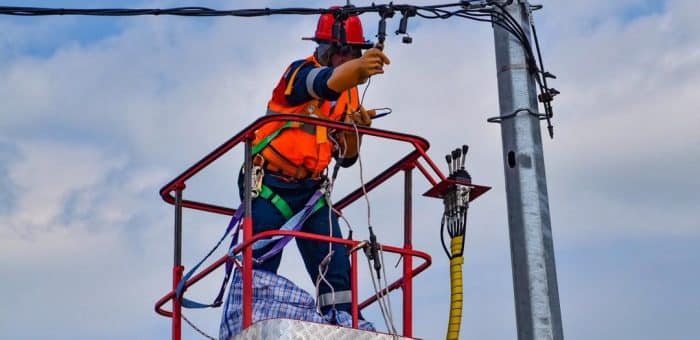 A person on a lift working on an electrical wire with a blue sky in the background