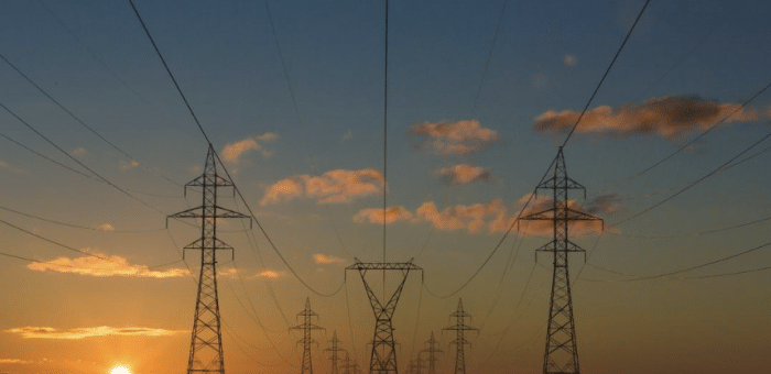 a high-ground photograph of three rows of transmission towers and power lines at sunset