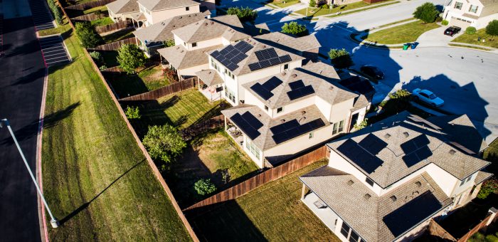 an aerial photograph of solar panels on a row of houses in a neighborhood